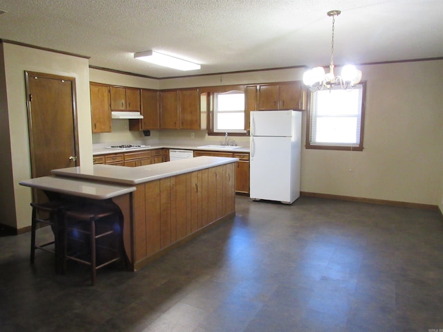 kitchen featuring white appliances, dark floors, brown cabinets, light countertops, and under cabinet range hood