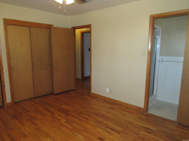 unfurnished bedroom with ensuite bath, a closet, a ceiling fan, and wood finished floors