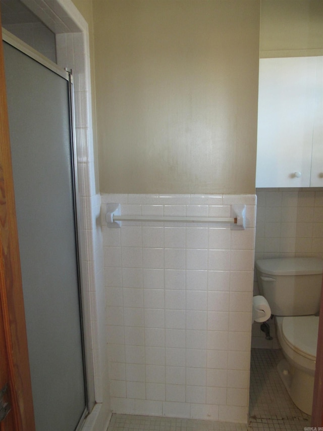 full bathroom featuring tile walls, toilet, a stall shower, wainscoting, and tile patterned floors