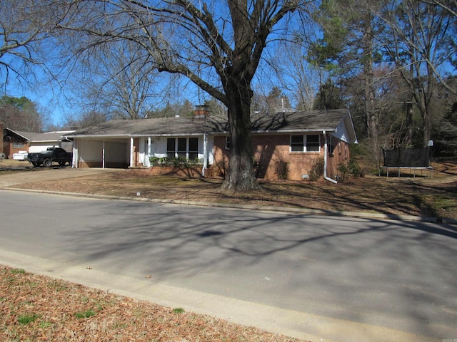 view of front of property with a garage, brick siding, driveway, a trampoline, and a chimney