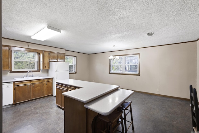 kitchen featuring light countertops, visible vents, brown cabinetry, a sink, and white appliances