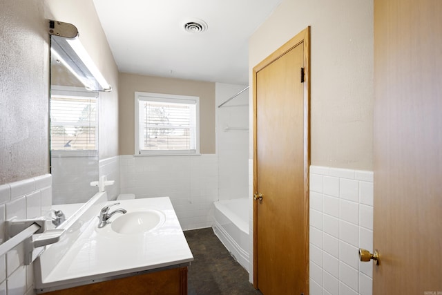 full bathroom featuring shower / bath combination, visible vents, a wainscoted wall, vanity, and tile walls