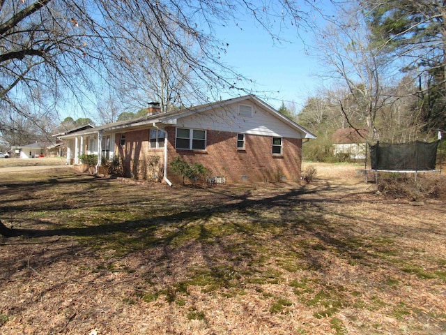 view of home's exterior featuring a lawn, a chimney, crawl space, a trampoline, and brick siding