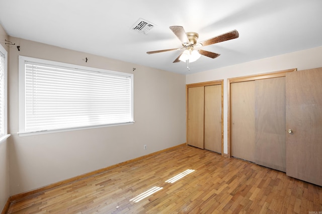 unfurnished bedroom with wood finished floors, visible vents, baseboards, and two closets