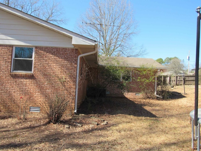 view of side of property with a yard, brick siding, crawl space, and fence