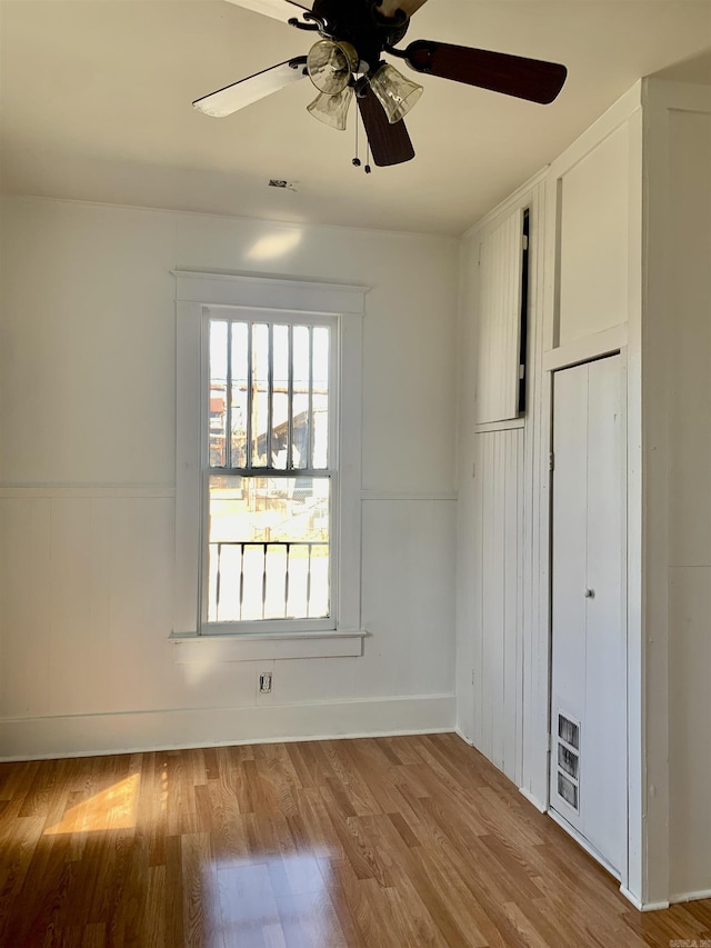 unfurnished bedroom featuring a wainscoted wall, a ceiling fan, and wood finished floors