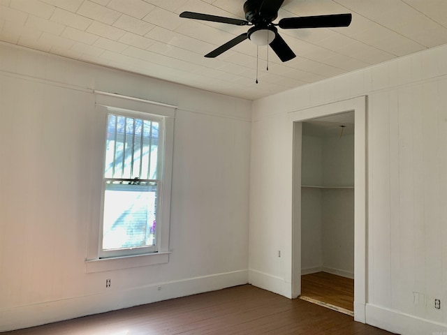 unfurnished bedroom with baseboards, ceiling fan, dark wood-type flooring, a walk in closet, and a closet