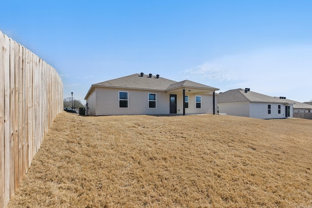 rear view of house featuring a lawn and fence