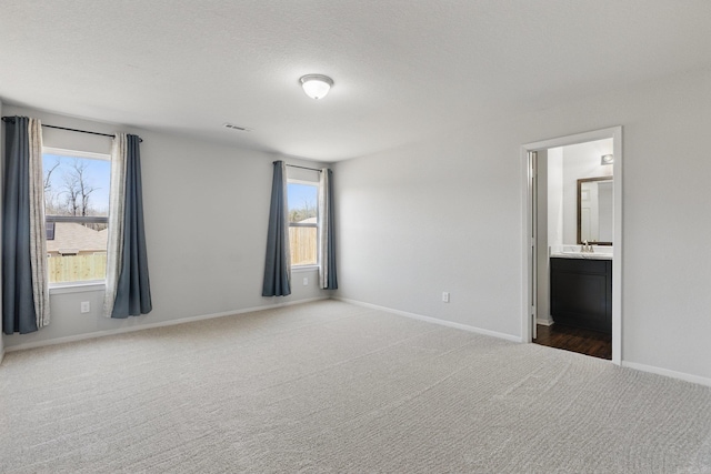 unfurnished bedroom featuring a textured ceiling, a sink, carpet flooring, visible vents, and baseboards