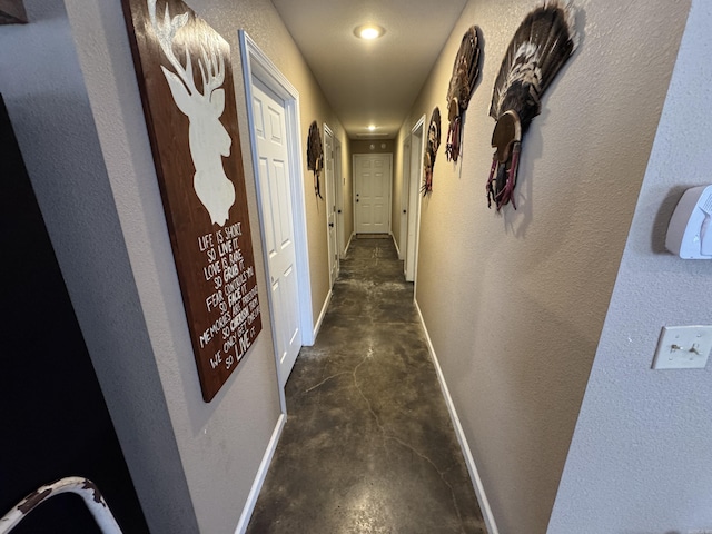 corridor with baseboards, concrete flooring, and a textured wall