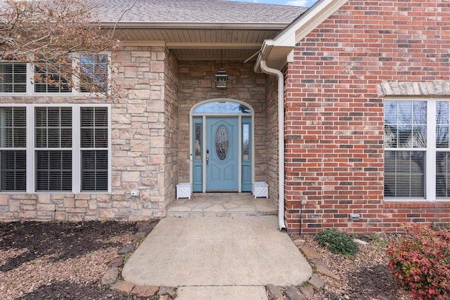 view of exterior entry featuring stone siding, brick siding, and roof with shingles