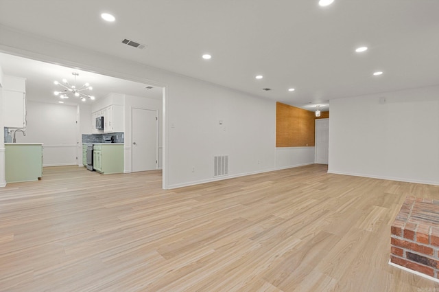 unfurnished living room featuring light wood-type flooring, an inviting chandelier, and visible vents