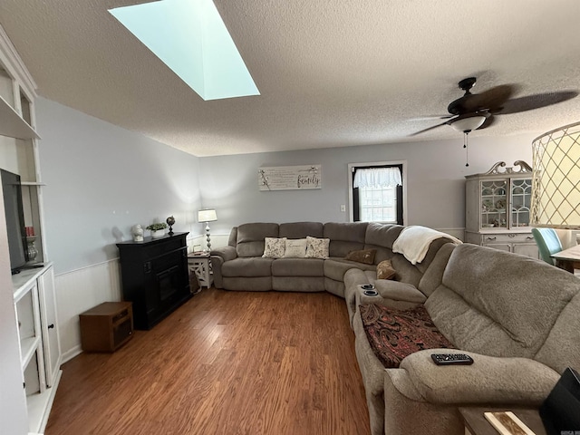 living room featuring a skylight, wainscoting, ceiling fan, wood finished floors, and a textured ceiling