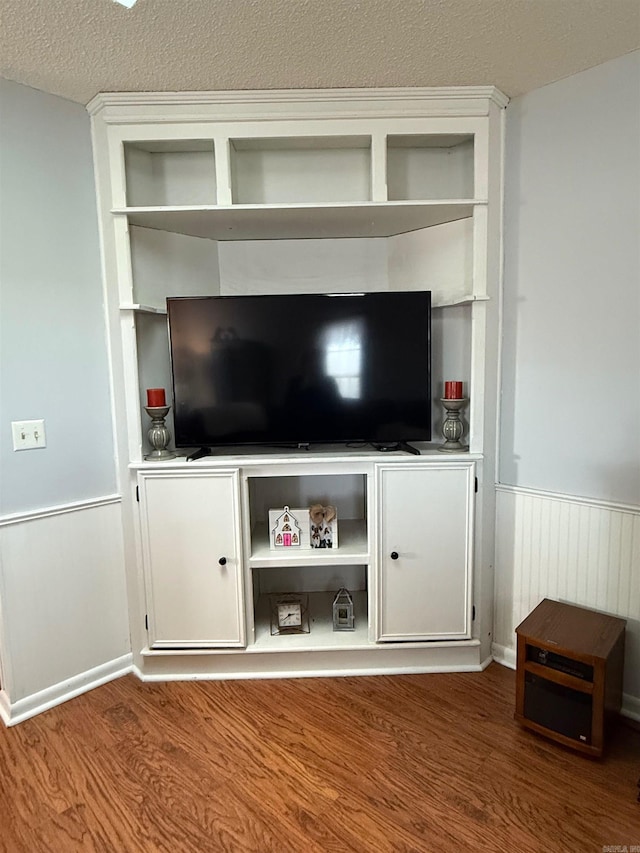 unfurnished living room with a textured ceiling, wainscoting, and wood finished floors