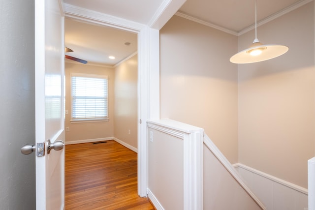 hallway with light wood-style flooring, visible vents, baseboards, and crown molding