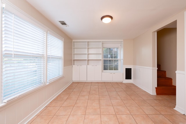 empty room featuring visible vents, a wainscoted wall, stairway, a decorative wall, and light tile patterned flooring