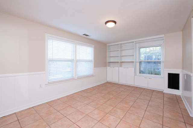 spare room featuring light tile patterned floors, built in shelves, wainscoting, and visible vents