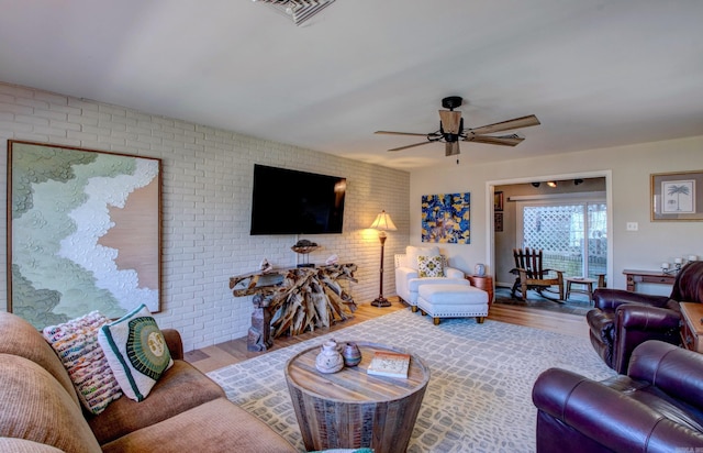 living area featuring a ceiling fan, brick wall, visible vents, and wood finished floors