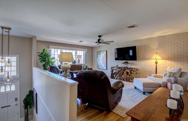 living room featuring brick wall, light wood finished floors, visible vents, and a ceiling fan