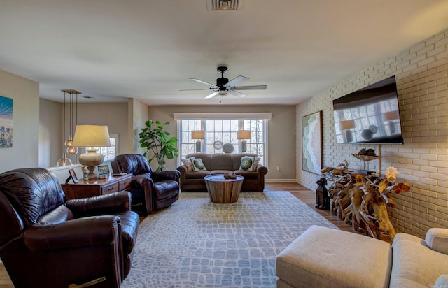 living room with baseboards, visible vents, a ceiling fan, brick wall, and wood finished floors