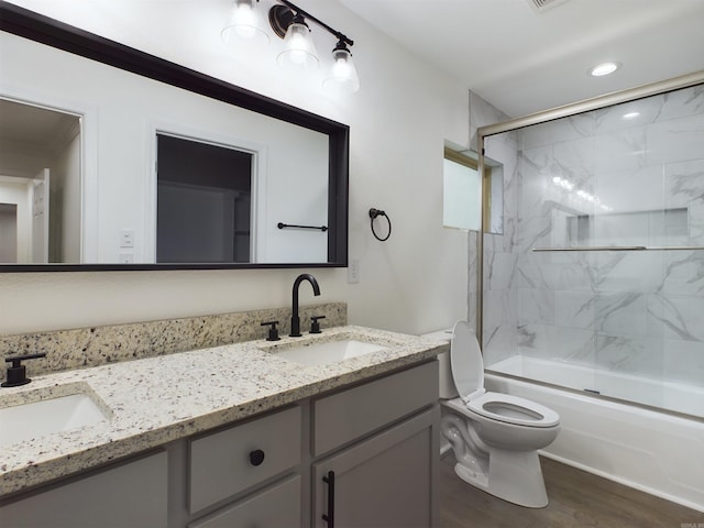 bathroom with double vanity, wood finished floors, shower / bath combination with glass door, and a sink