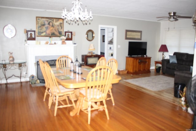 dining area featuring ceiling fan with notable chandelier, wood finished floors, crown molding, and a fireplace