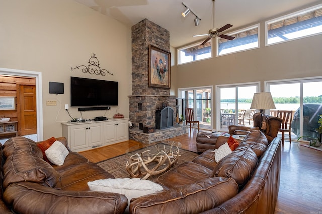 living area with light wood-type flooring, plenty of natural light, a stone fireplace, and a towering ceiling