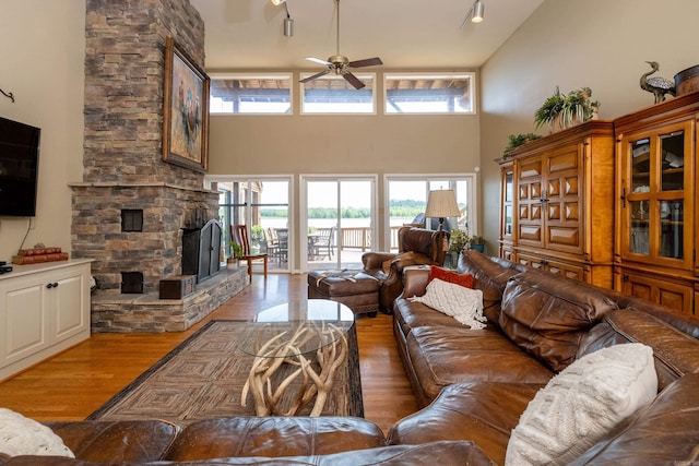 living room featuring ceiling fan, a stone fireplace, wood finished floors, and a high ceiling