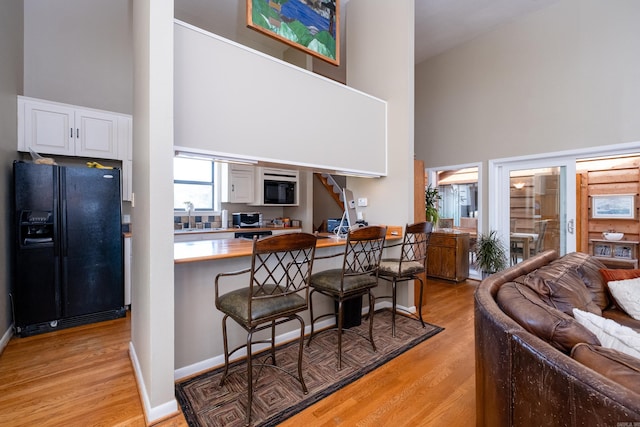 kitchen featuring a breakfast bar area, black refrigerator with ice dispenser, light wood-type flooring, white cabinetry, and high vaulted ceiling