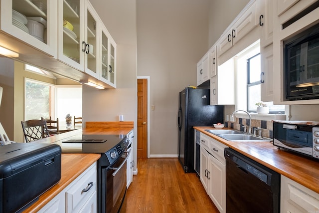 kitchen featuring black appliances, light wood-style floors, wooden counters, and a sink