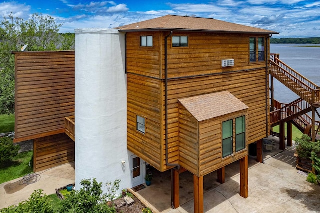 rear view of house featuring roof with shingles, stairway, and a patio area