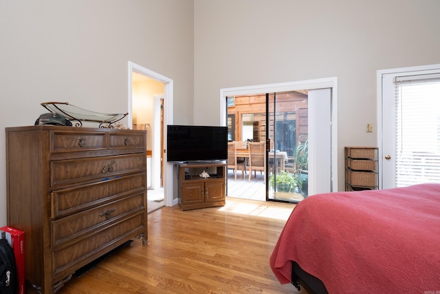 bedroom with access to exterior, light wood-style floors, and a towering ceiling