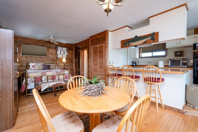 dining space featuring light wood-style floors, ceiling fan, and wooden walls