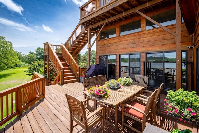 deck with outdoor dining space, a yard, and stairs