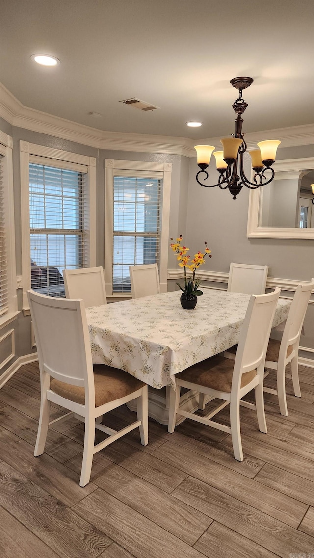 dining room with ornamental molding, wood finished floors, visible vents, and a notable chandelier