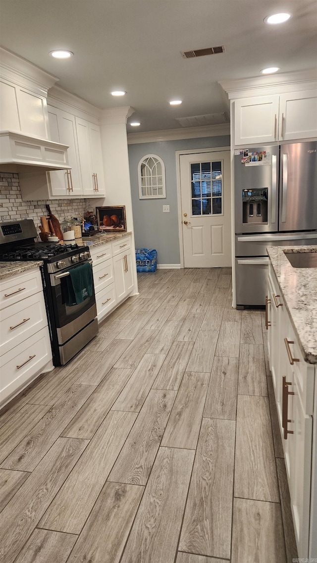 kitchen with visible vents, ornamental molding, stainless steel appliances, premium range hood, and backsplash