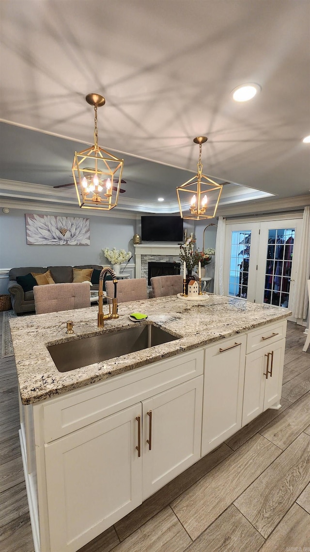 kitchen with a sink, white cabinetry, open floor plan, wood tiled floor, and an inviting chandelier