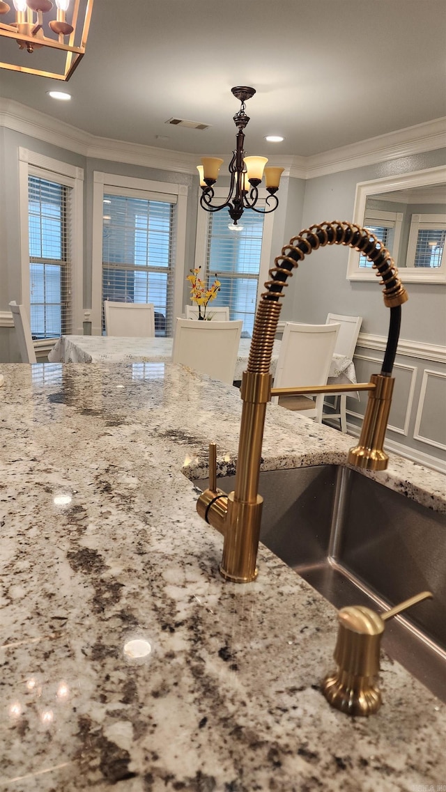 room details with a chandelier, light stone counters, a sink, ornamental molding, and decorative light fixtures