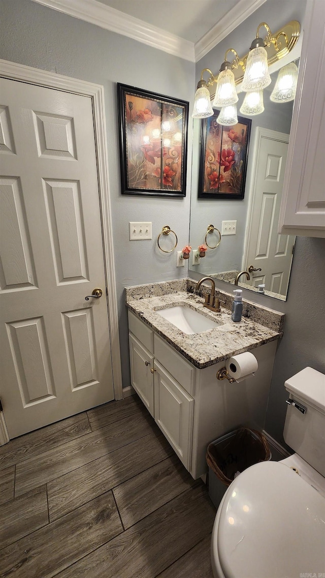 half bath featuring vanity, ornamental molding, wood finished floors, and toilet