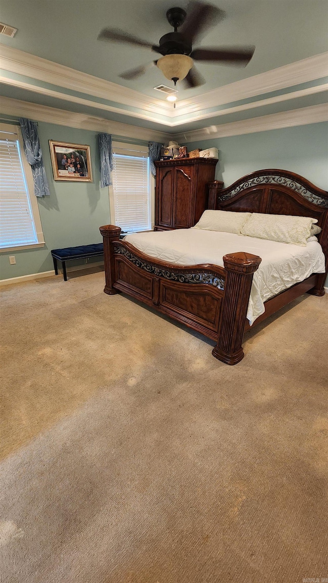 carpeted bedroom featuring a tray ceiling, crown molding, visible vents, a ceiling fan, and baseboards