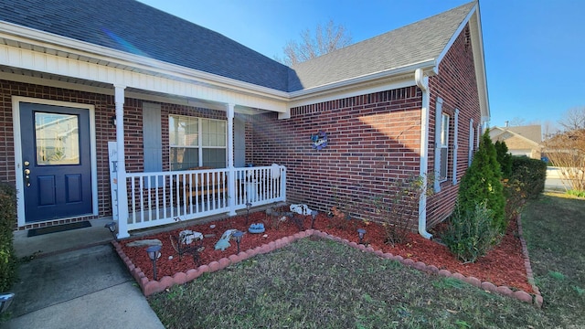 property entrance with a porch, roof with shingles, and brick siding