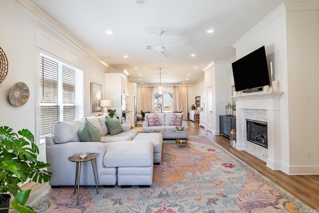 living area featuring baseboards, a high end fireplace, wood finished floors, crown molding, and recessed lighting