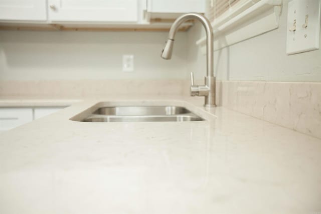 details with light stone counters, a sink, and white cabinetry