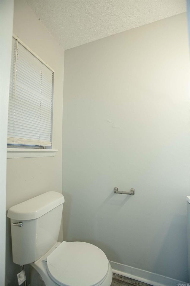 bathroom with baseboards, a textured ceiling, toilet, and wood finished floors