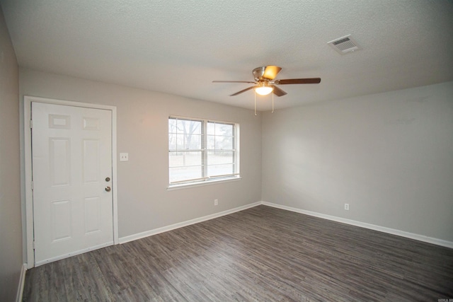 unfurnished room with a textured ceiling, dark wood-type flooring, a ceiling fan, visible vents, and baseboards