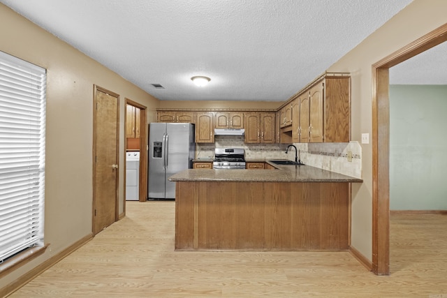 kitchen with appliances with stainless steel finishes, a sink, a peninsula, washer / dryer, and under cabinet range hood