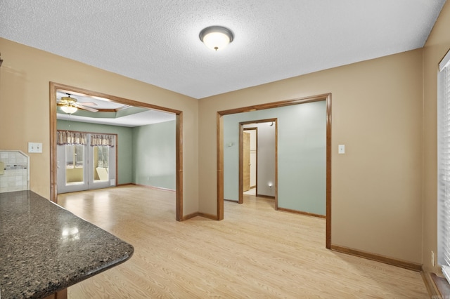 unfurnished room with light wood-style flooring, baseboards, a textured ceiling, and french doors