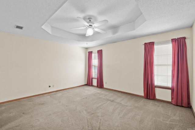 empty room featuring a tray ceiling, visible vents, carpet flooring, ceiling fan, and baseboards