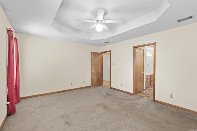 unfurnished bedroom featuring visible vents, baseboards, ensuite bathroom, a tray ceiling, and carpet flooring