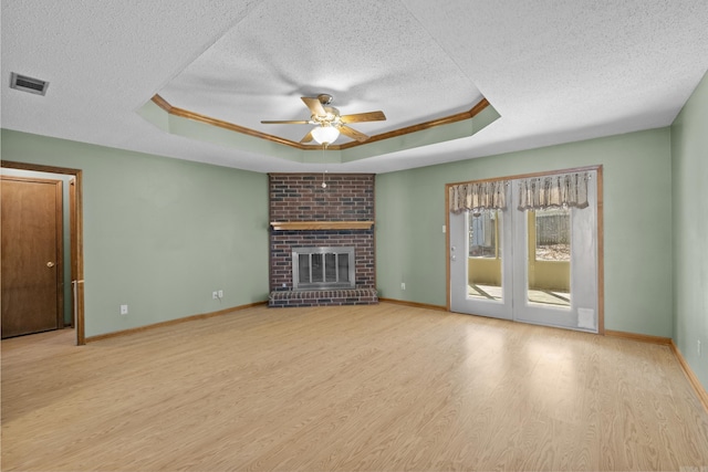 unfurnished living room featuring a brick fireplace, a raised ceiling, visible vents, and wood finished floors